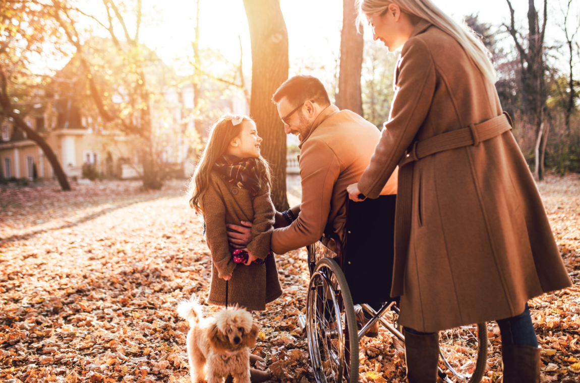 man who uses a wheelchair smiles at a young girl while a woman stands behind them