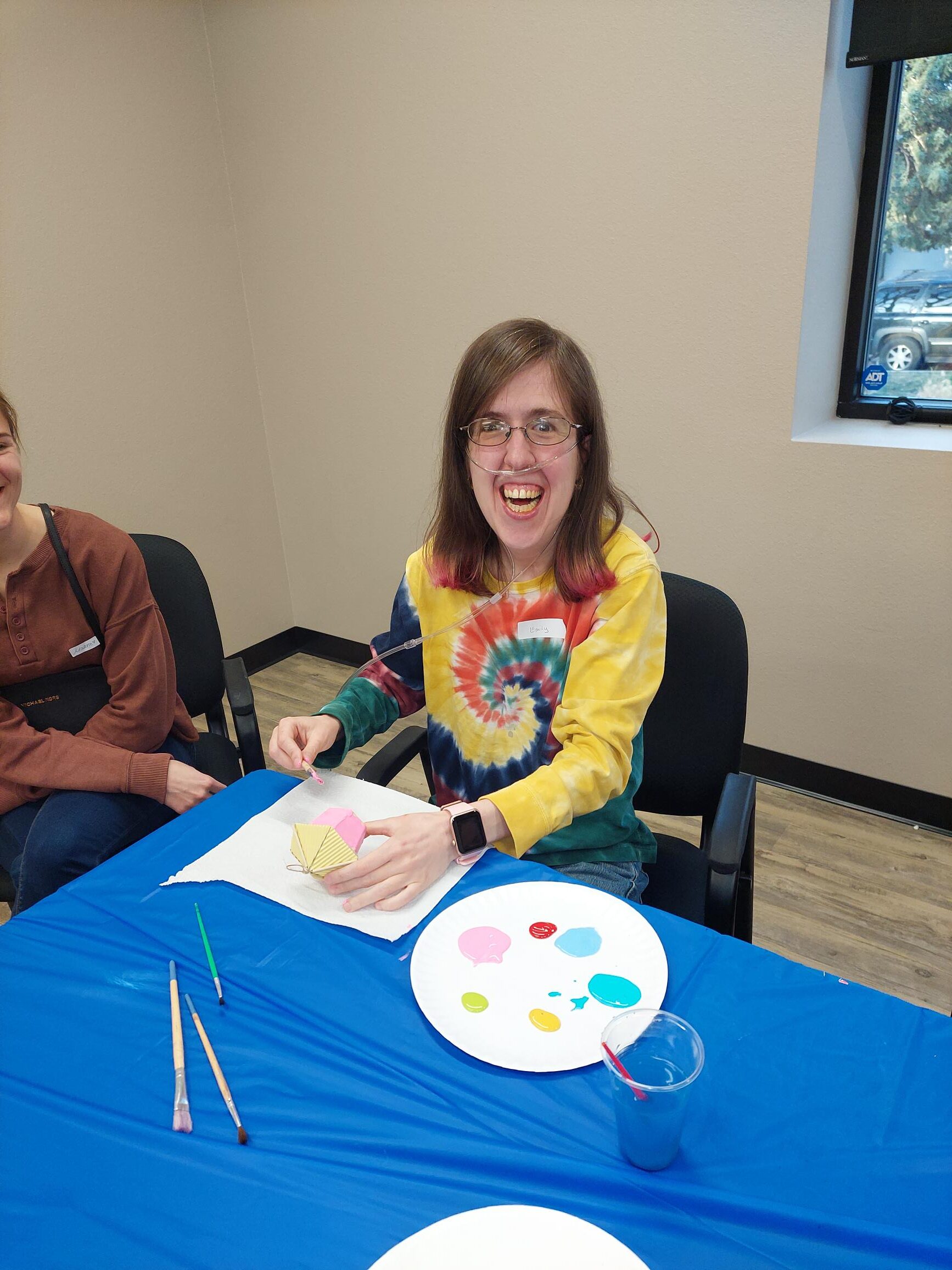 young adult smiling at the viewer while painting a small wooden object