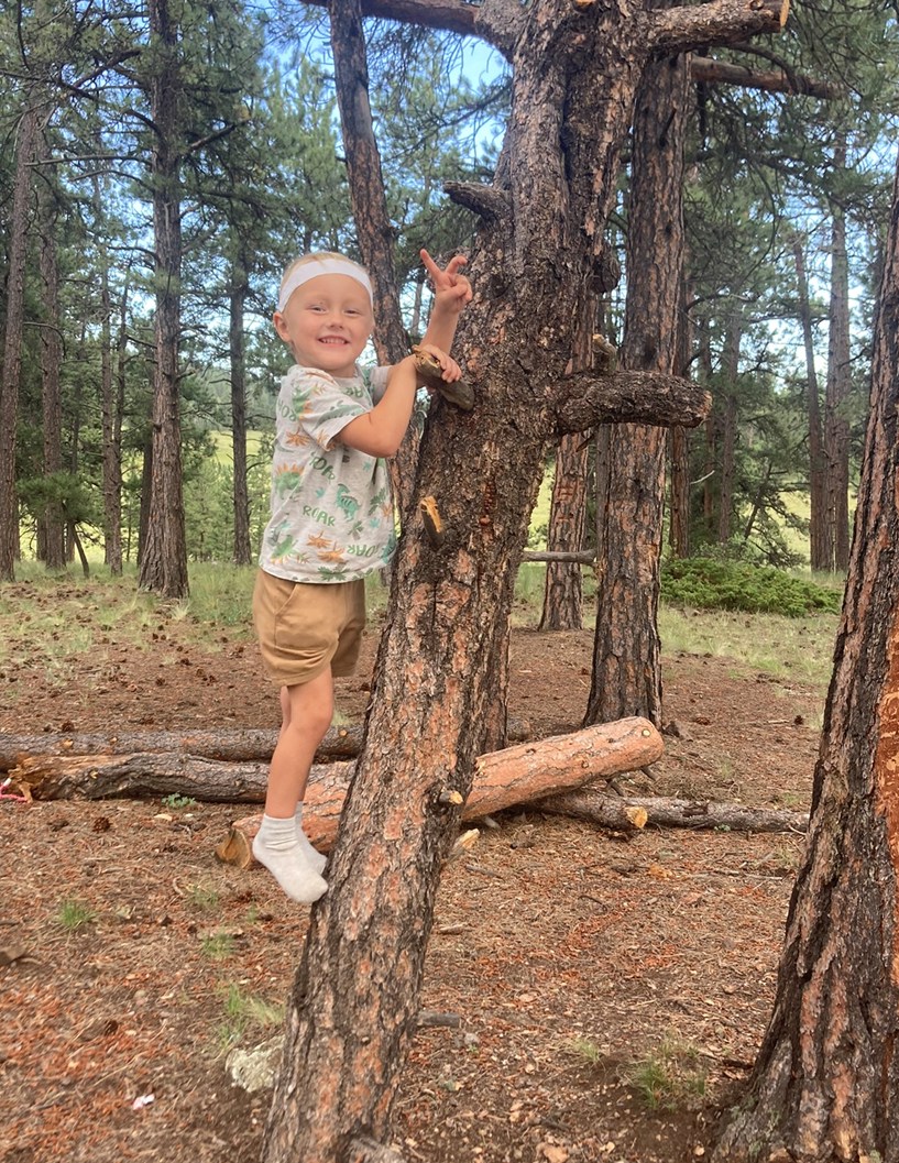 toddler outside climbing a tree and smiling at the viewer