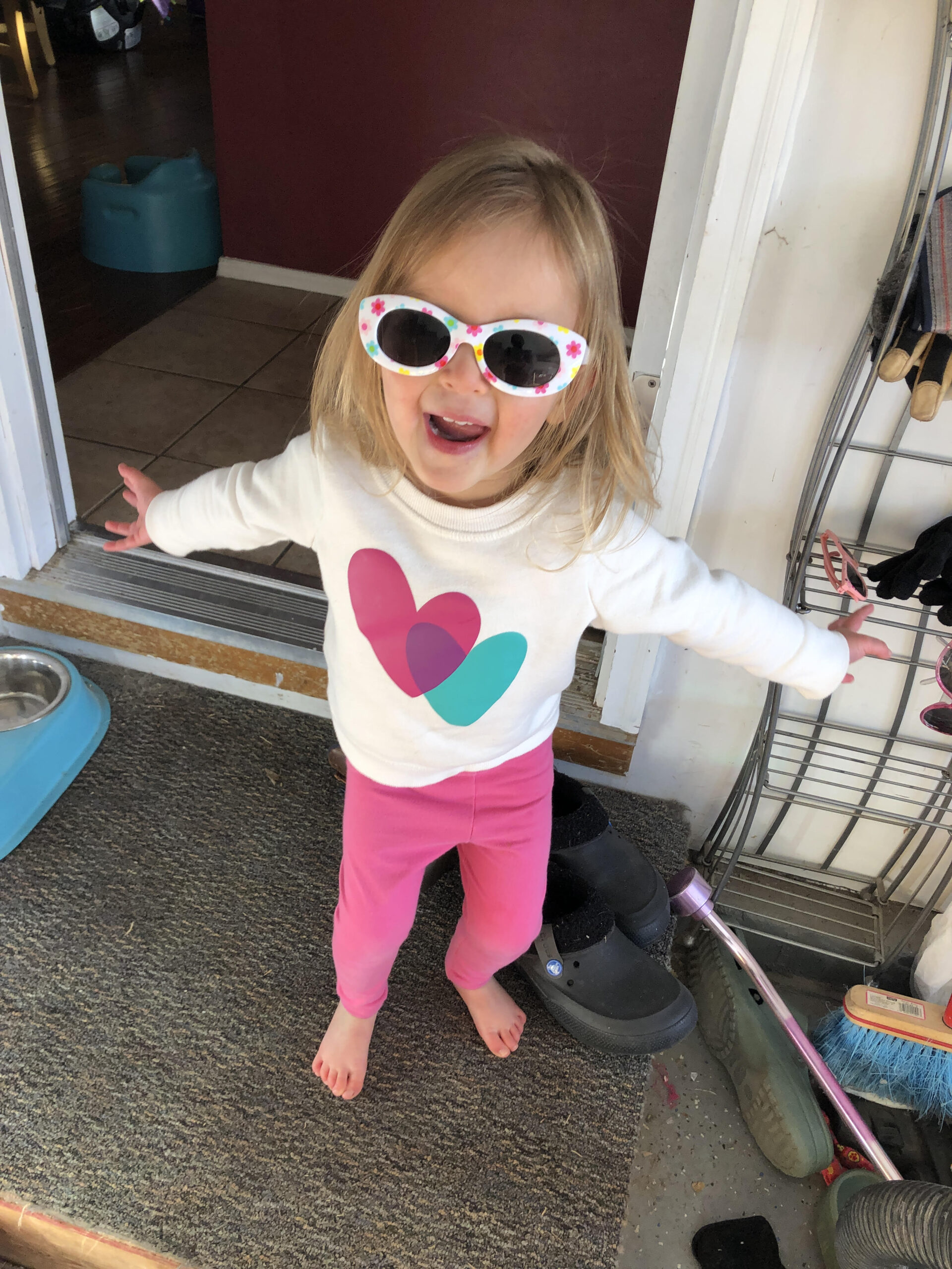 toddler wearing sunglasses with arms outstretched smiling at viewer