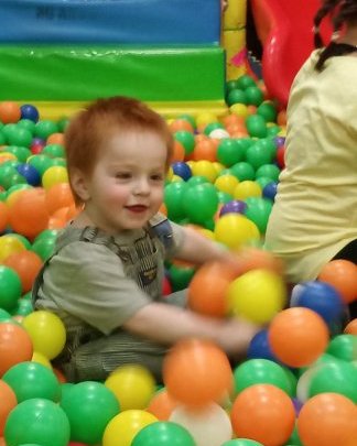 toddler smiling while playing in a ball pit with multicolored plastic balls