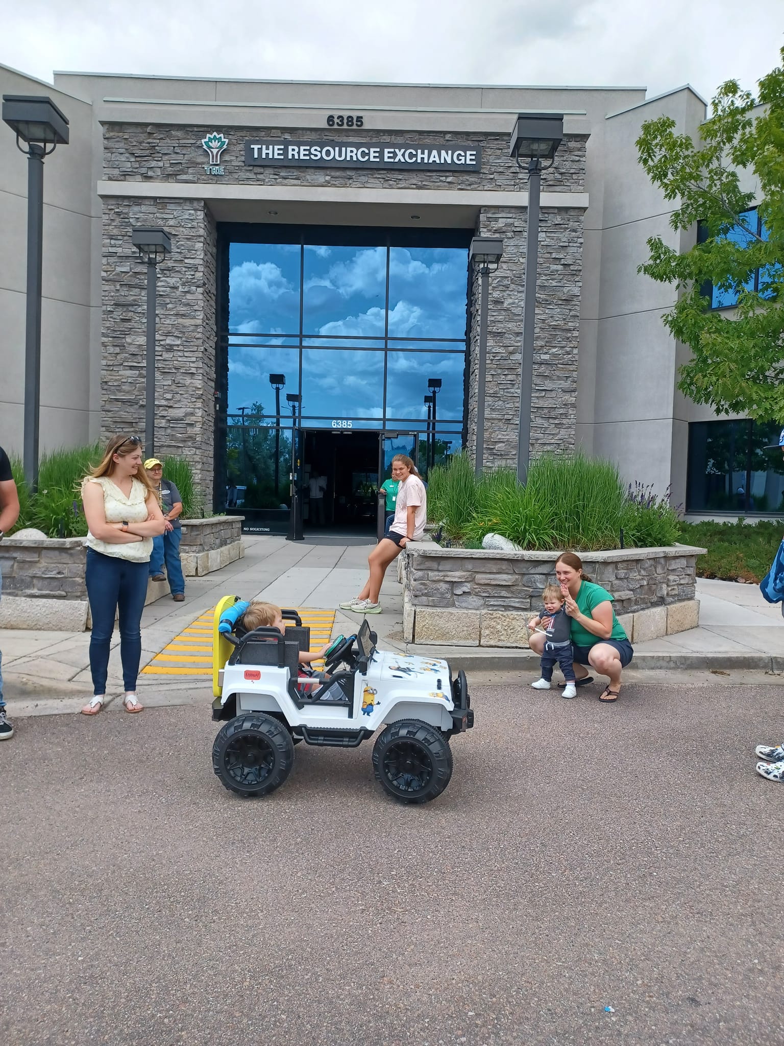 toddler rides a miniature jeep in front of The Resource Exchange building