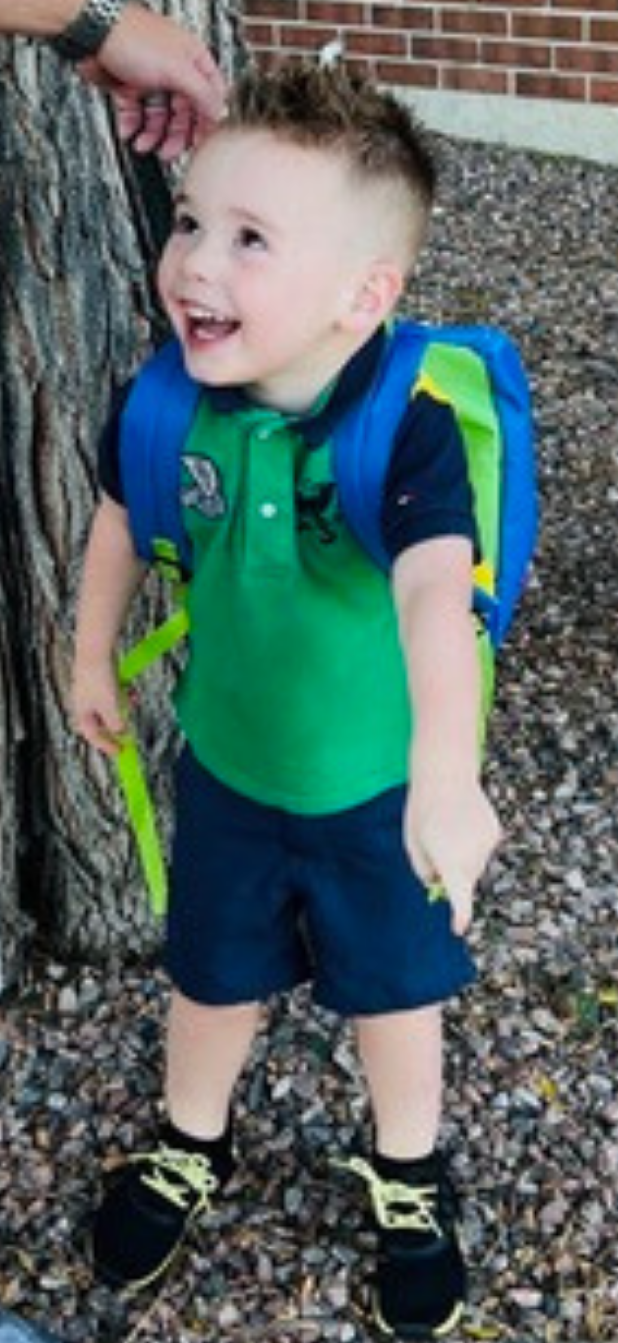 toddler wearing a backpack and colorful clothes smiles while standing outside
