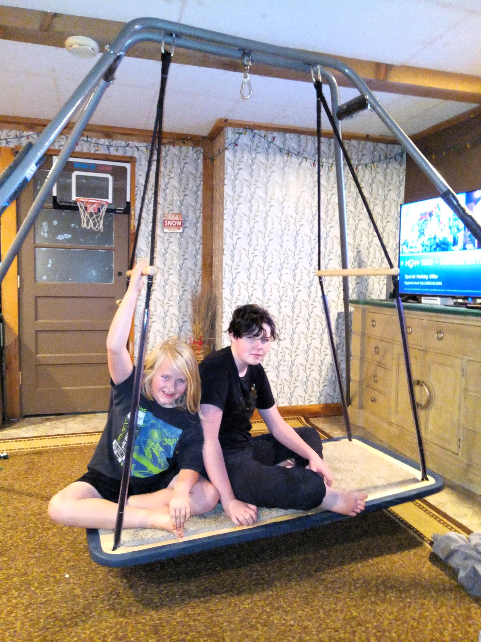 two young adults sit on a sensory swing suspended from the ceiling