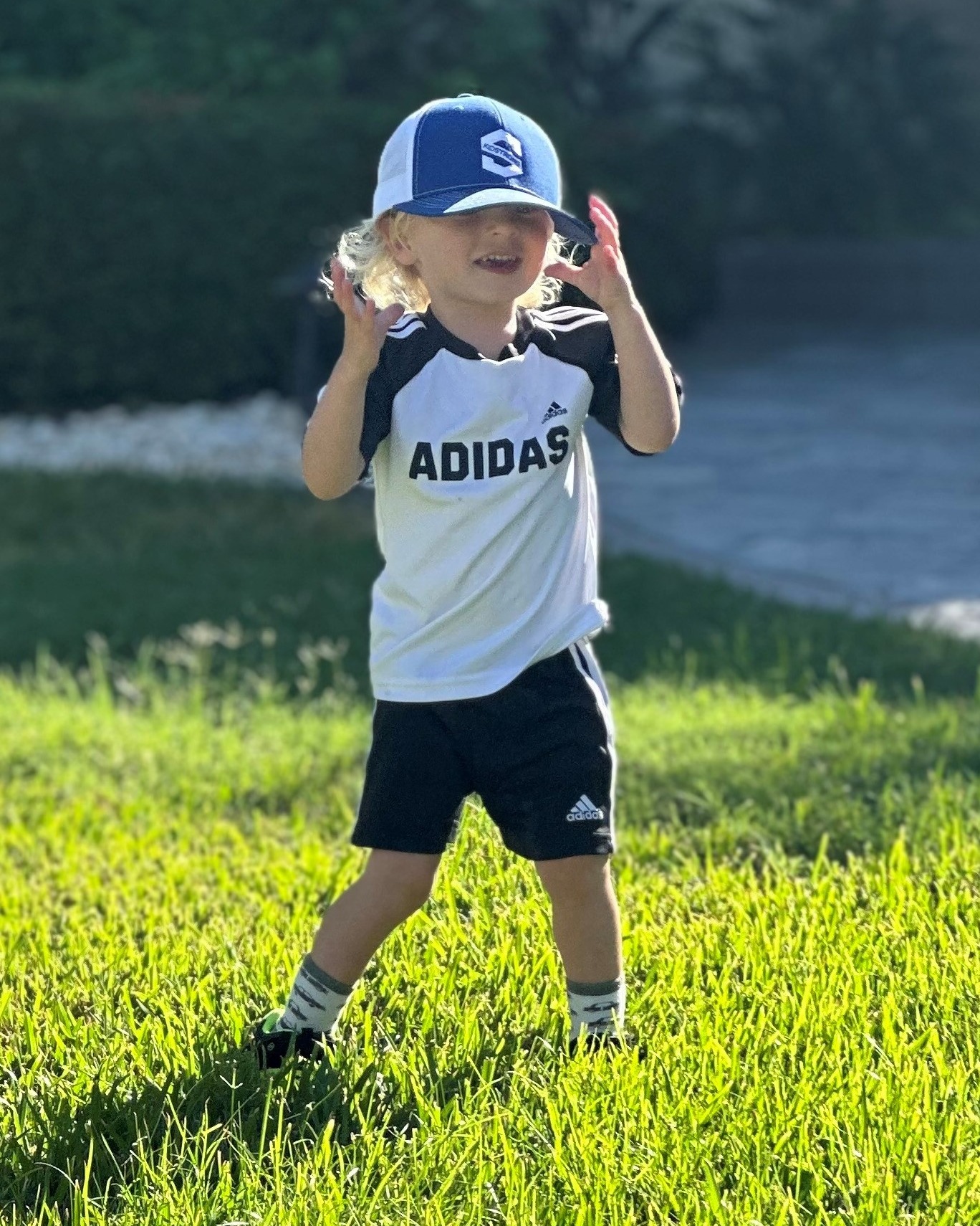 toddler wearing a blue baseball cap and summer clothes while standing outside in the grass on a sunny day
