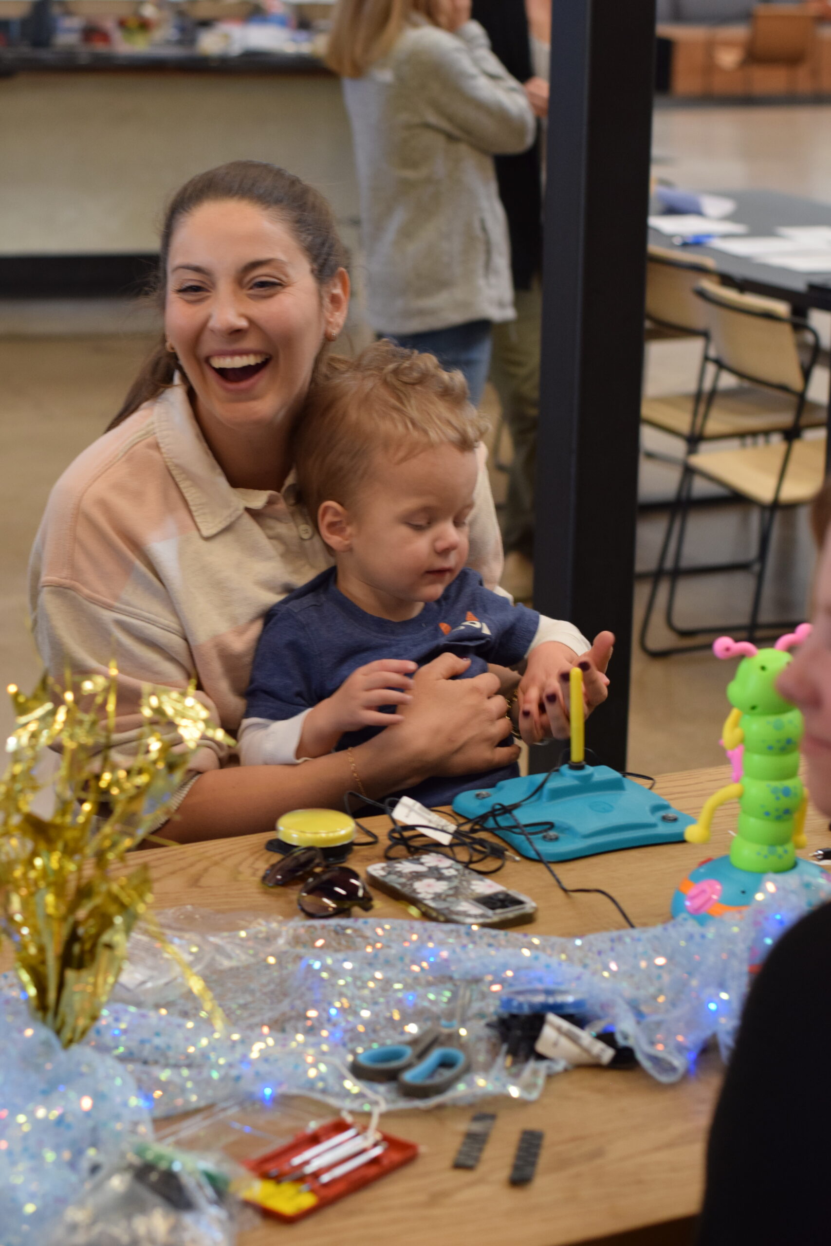A mother beams with joy while holding her child as he uses a switch to operate his new toy